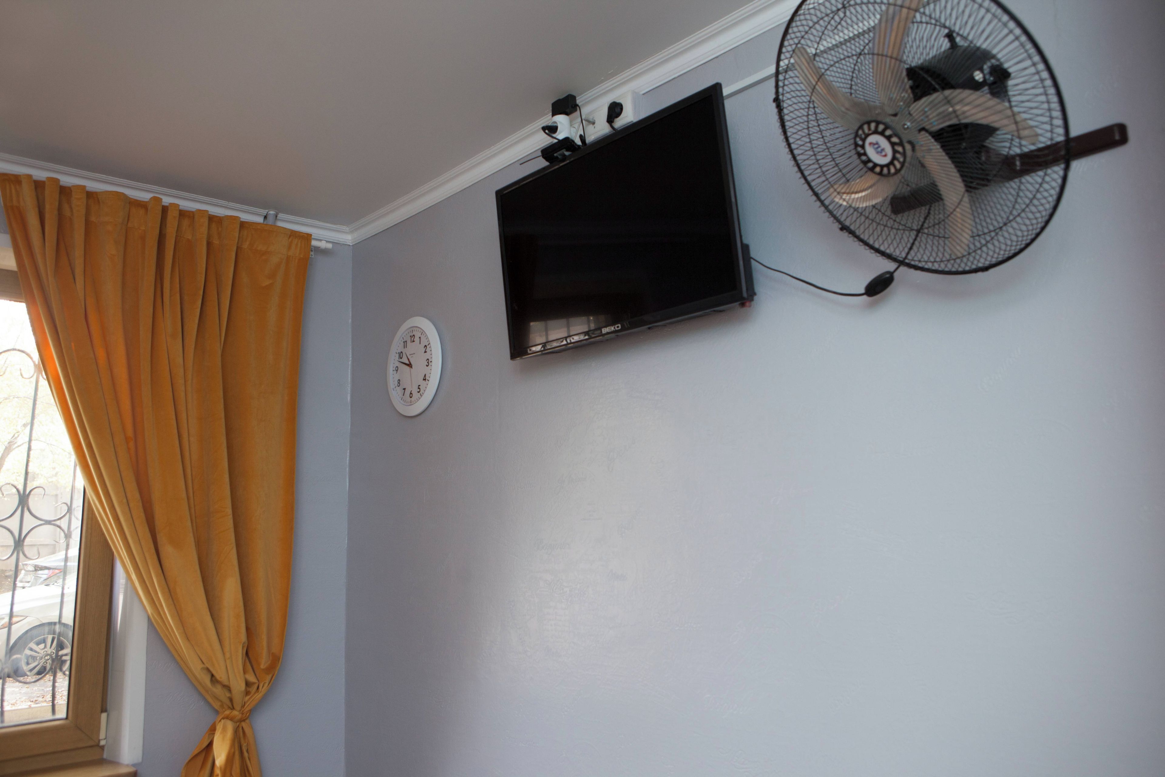 A room with a wall-mounted TV, a clock, and a ceiling fan.