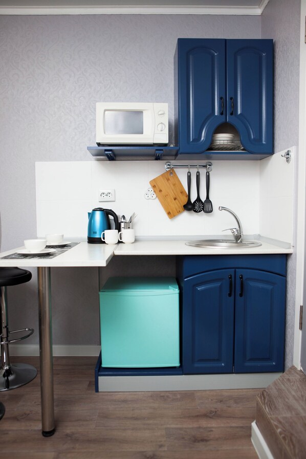 A compact kitchen with a microwave, a sink, and a bar stool.