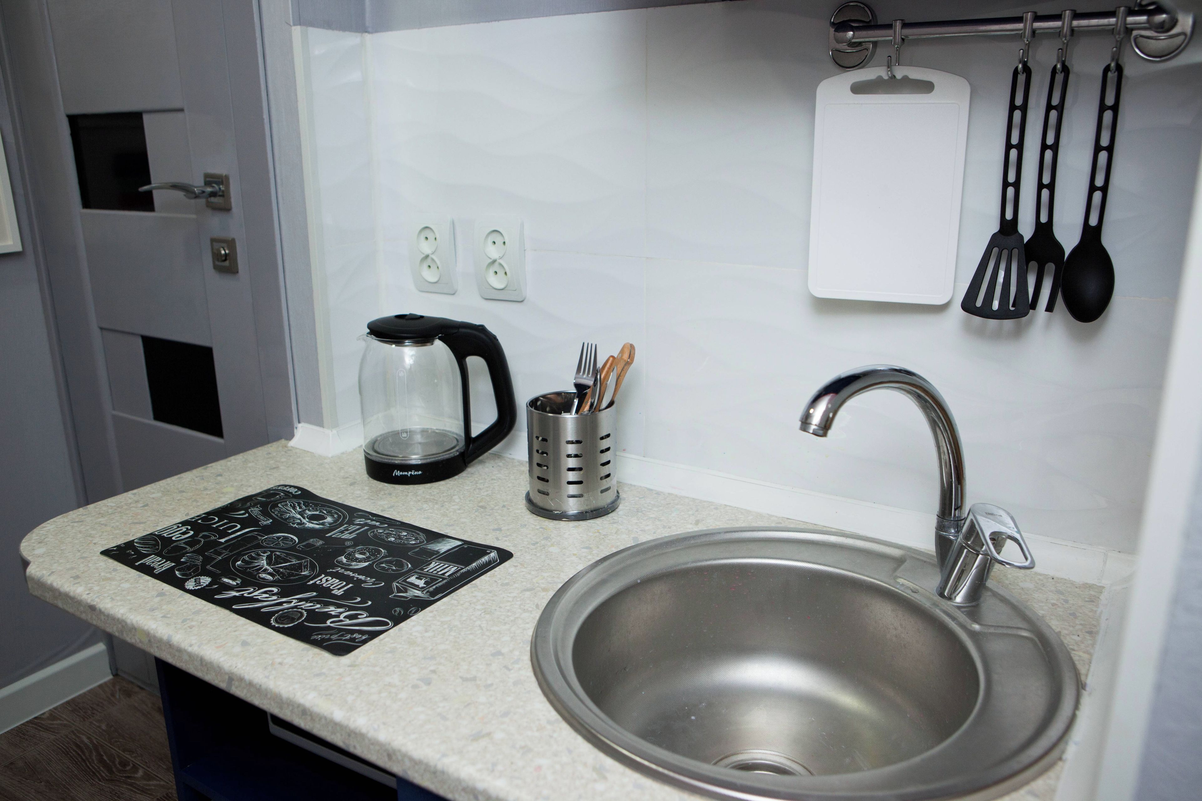 A kitchen with a stainless steel sink, a coffee maker, a knife holder, and a black and white placemat on the countertop.