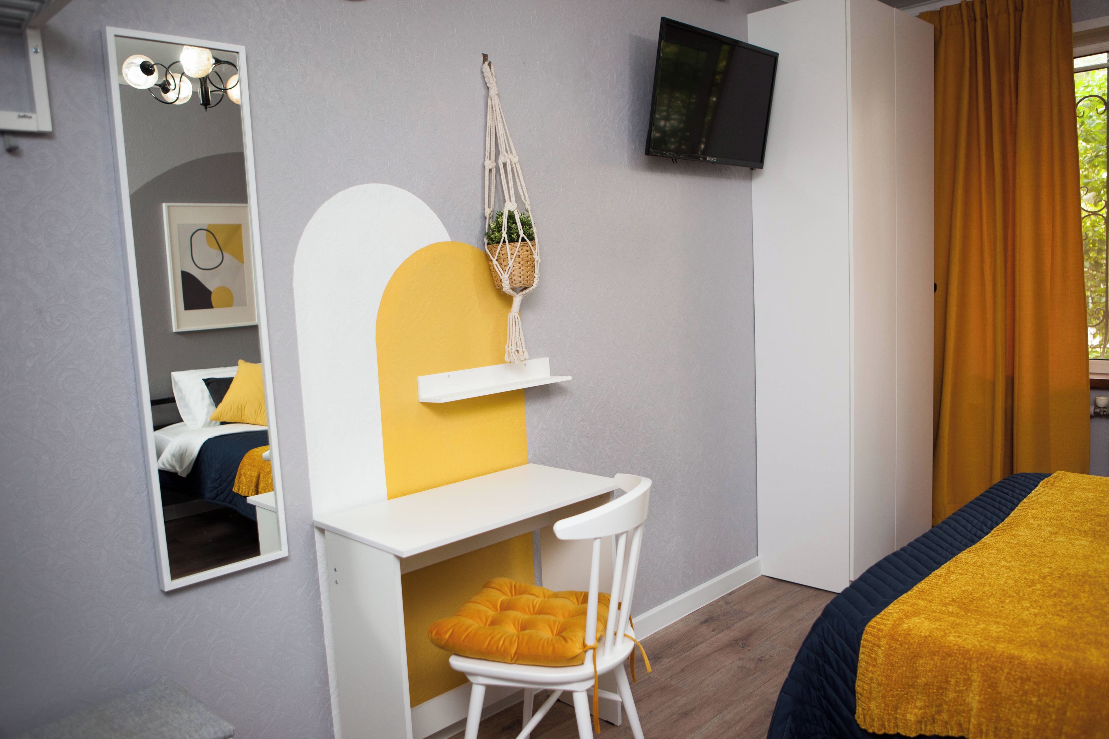 Una camera d'albergo con un letto, una scrivania con una sedia, uno specchio, una televisione e una finestra con tende.