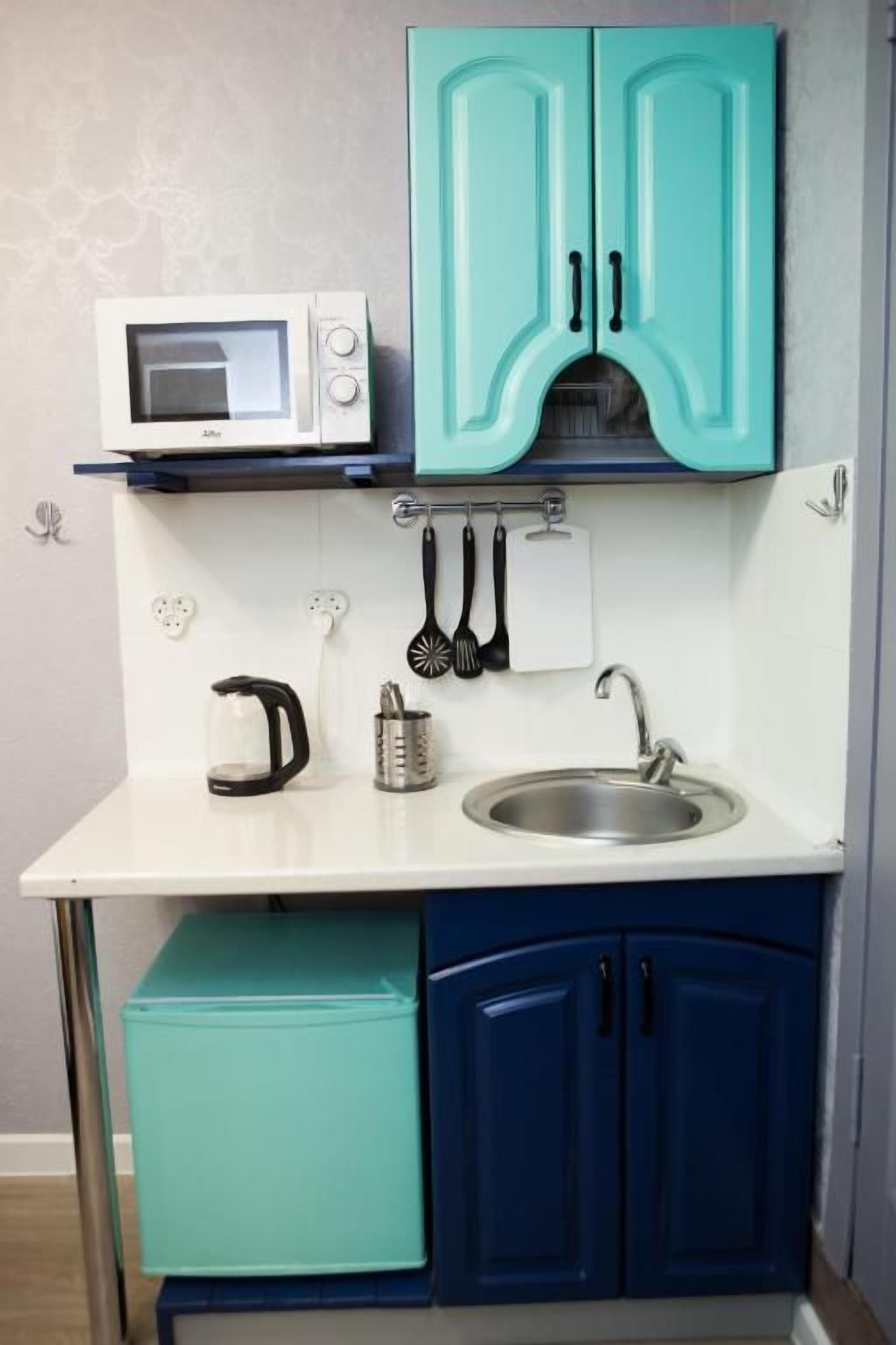 Una cucina compatta con pensili color acquamarina, un piano di lavoro bianco, un forno a microonde, un bollitore, una macchina da caffè e un lavello.
