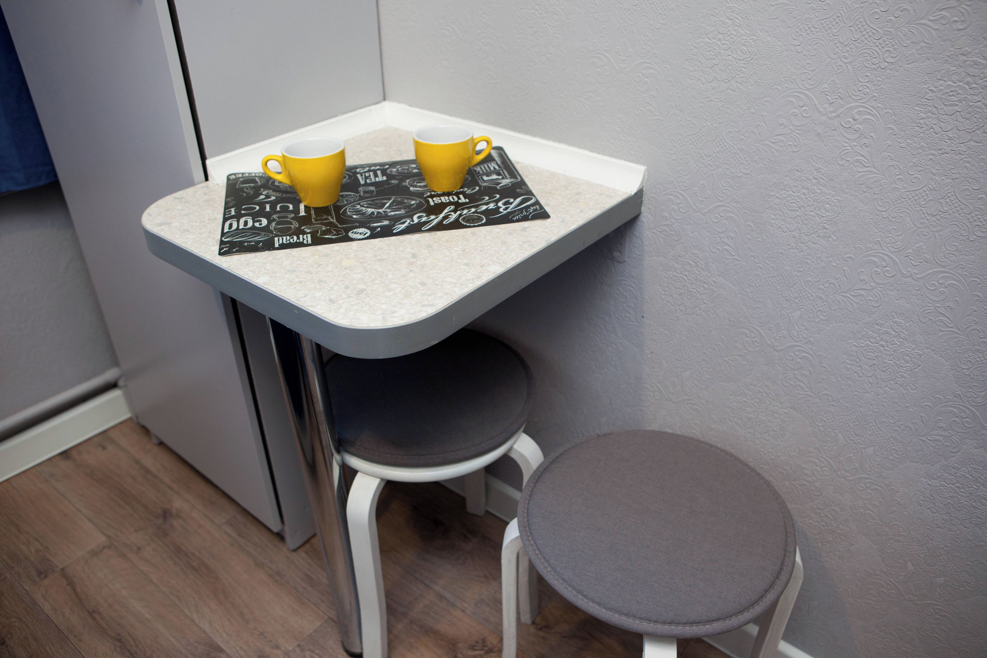 Pequeña cocina con encimera blanca, dos tazas amarillas y un mantel individual negro con texto.