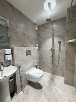 A modern bathroom with a marble floor, a toilet, a sink, a shower, and a hand dryer.