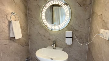 Un baño con pared de mármol, un espejo redondo con luces, un lavamanos y un perchero para toallas.