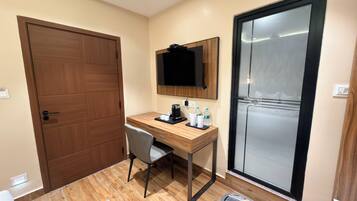 A hotel room with a wooden desk, a chair, a flat-screen TV mounted on the wall, a sliding glass door, and a small rug on the floor.
