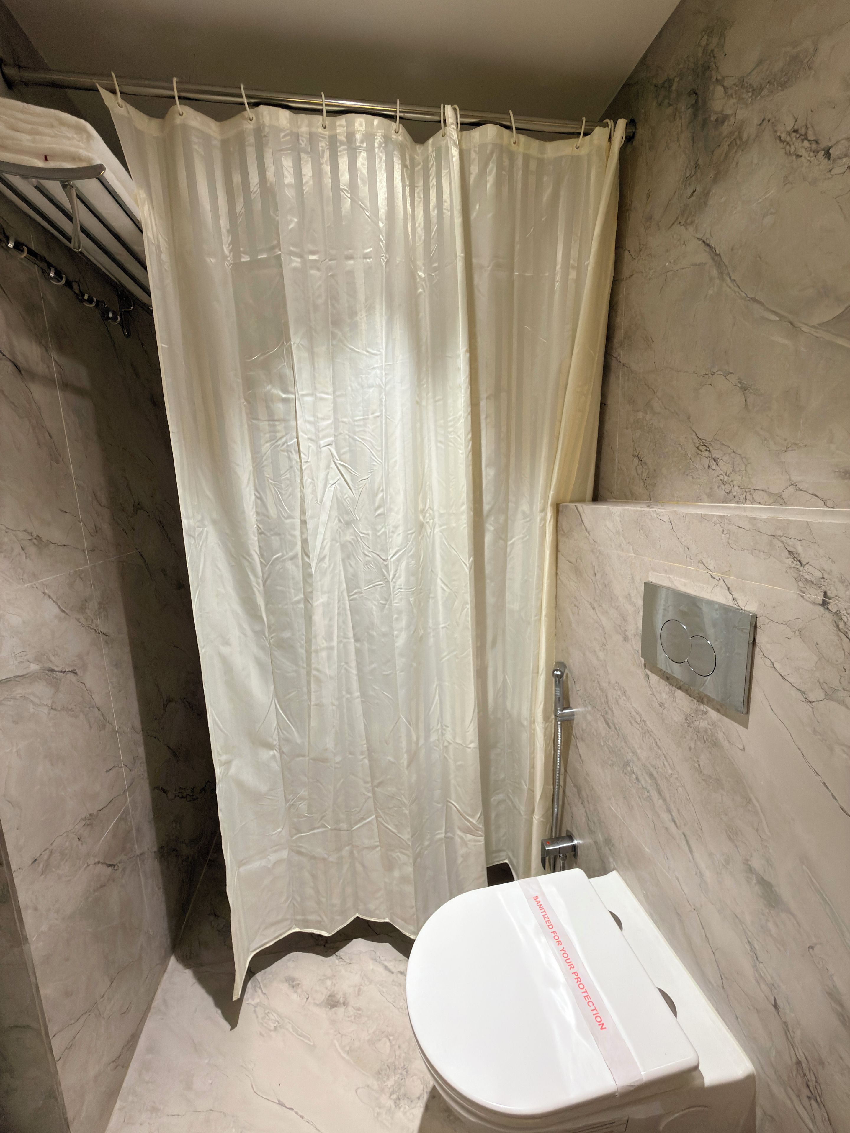 A bathroom with a shower curtain, a toilet, and a marble wall.