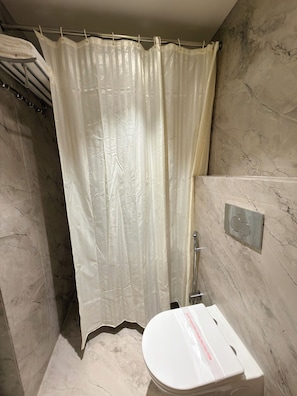 A bathroom with a shower curtain, a toilet, and a marble wall.