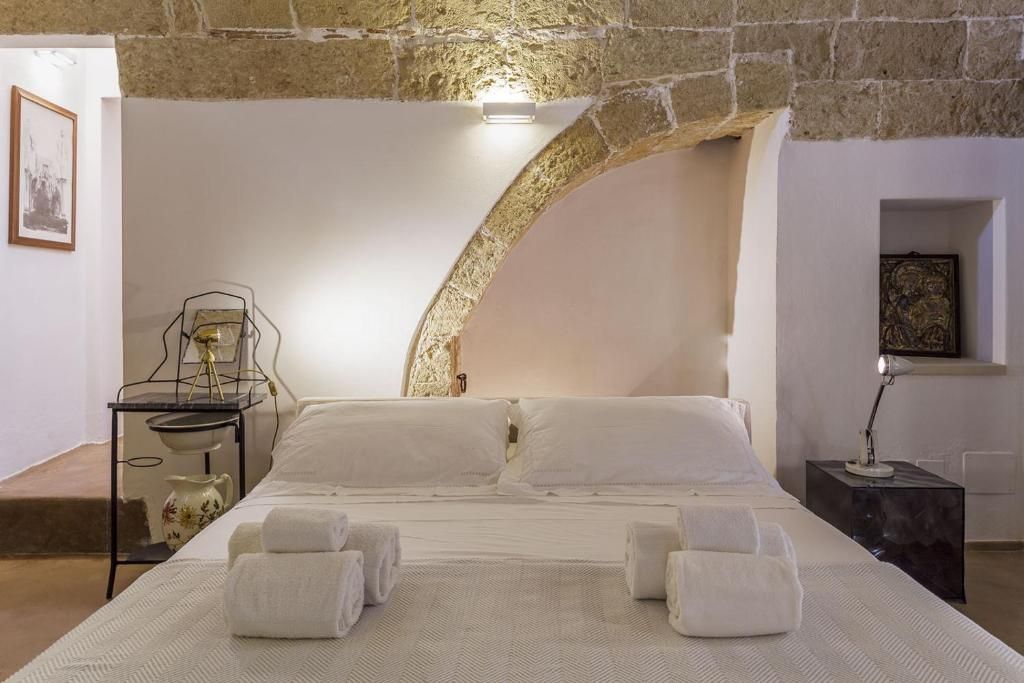 A bedroom with a stone arch, a bed with white linens, a bedside table with a lamp, and a framed picture on the wall.