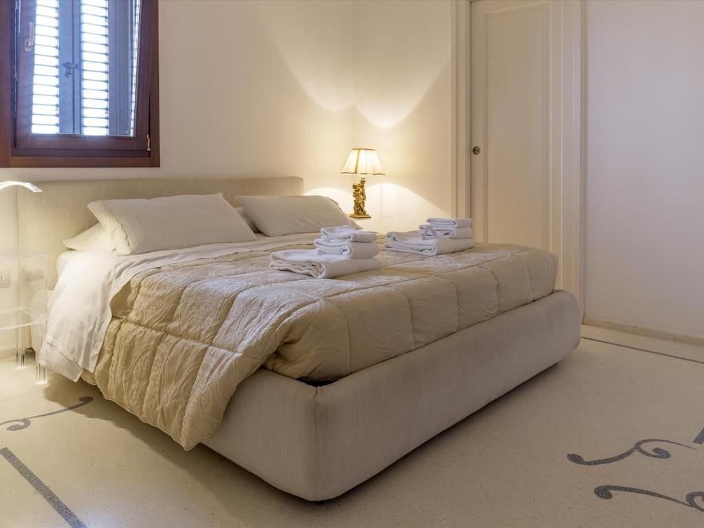 Una cama bien hecha con cabecera, lámpara de noche y toallas dobladas sobre la cama.