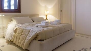 Una cama bien hecha con cabecera, lámpara de noche y toallas dobladas sobre la cama.