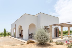 Un edificio blanco con un patio cubierto y un jardín con arbustos y flores.