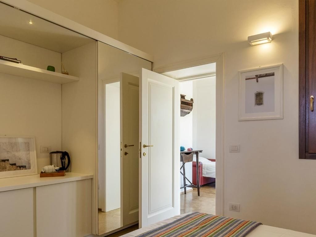 Un dormitorio con cama, mesita de noche, espejo y puerta que da a otra habitación.