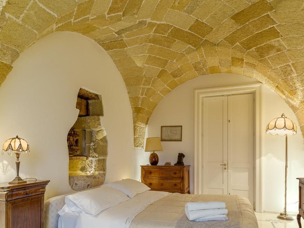 Een slaapkamer met een stenen plafond, een bed met witte lakens, een houten dressoir en twee lampen.