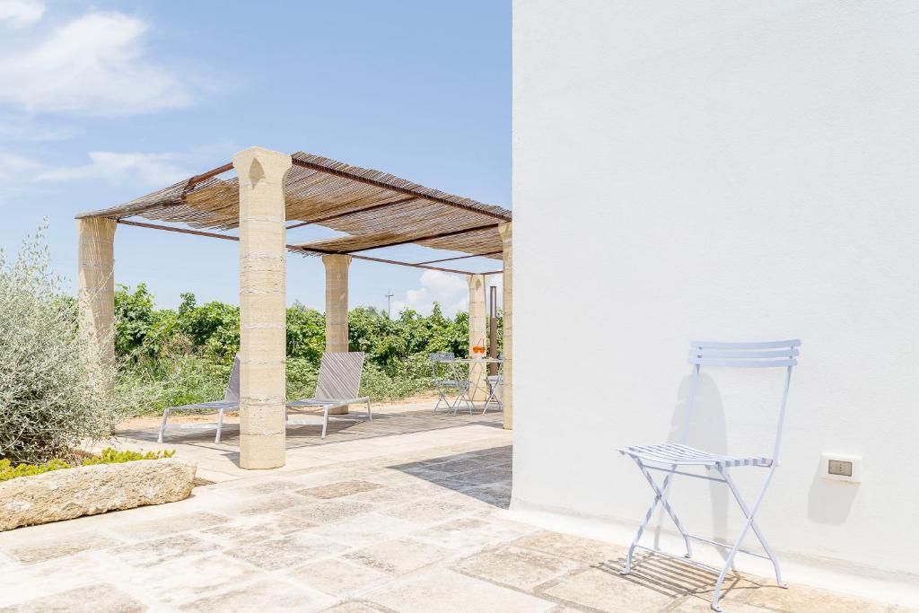 Ein Terrassenbereich im Freien mit einer Pergola, Sitzgelegenheiten und einer weißen Wand.