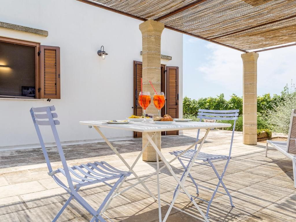 An outdoor patio with a table and chairs, a wooden pergola, and a view of greenery in the background.