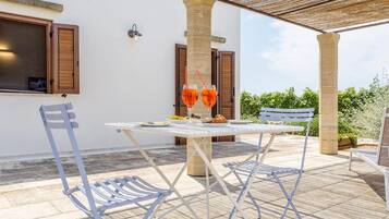 An outdoor patio with a table and chairs, a wooden pergola, and a view of greenery in the background.