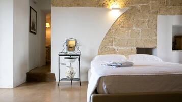 A bedroom with a stone wall, a bed with white linens, a bedside table with a lamp, and a small decorative item on the bed.