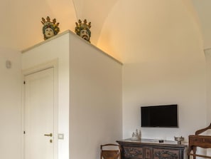 A room with a white door, a flat-screen TV mounted on the wall, and a wooden cabinet with decorative carvings. - TenutaYala - Residenza Agrituristica (Parabita)