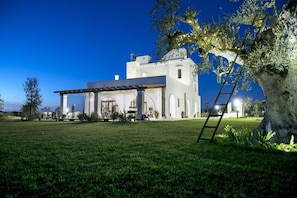 A large white building with a covered patio area, surrounded by a well-maintained lawn and a large tree. - TenutaYala - Residenza Agrituristica (Parabita)