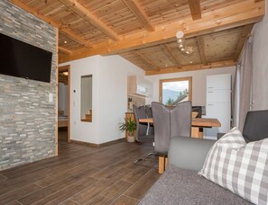 A modern interior with a stone wall, wooden ceiling beams, a dining area with chairs, a sofa, and a view of mountains through a window. - With 3 Bedrooms (Velturno)
