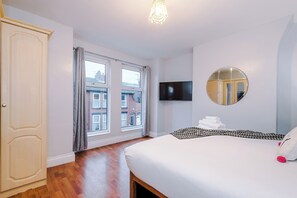 Ein Hotelzimmer mit einem großen Bett, einem Flachbildfernseher, einem runden Spiegel und Blick auf Gebäude durch das Fenster.