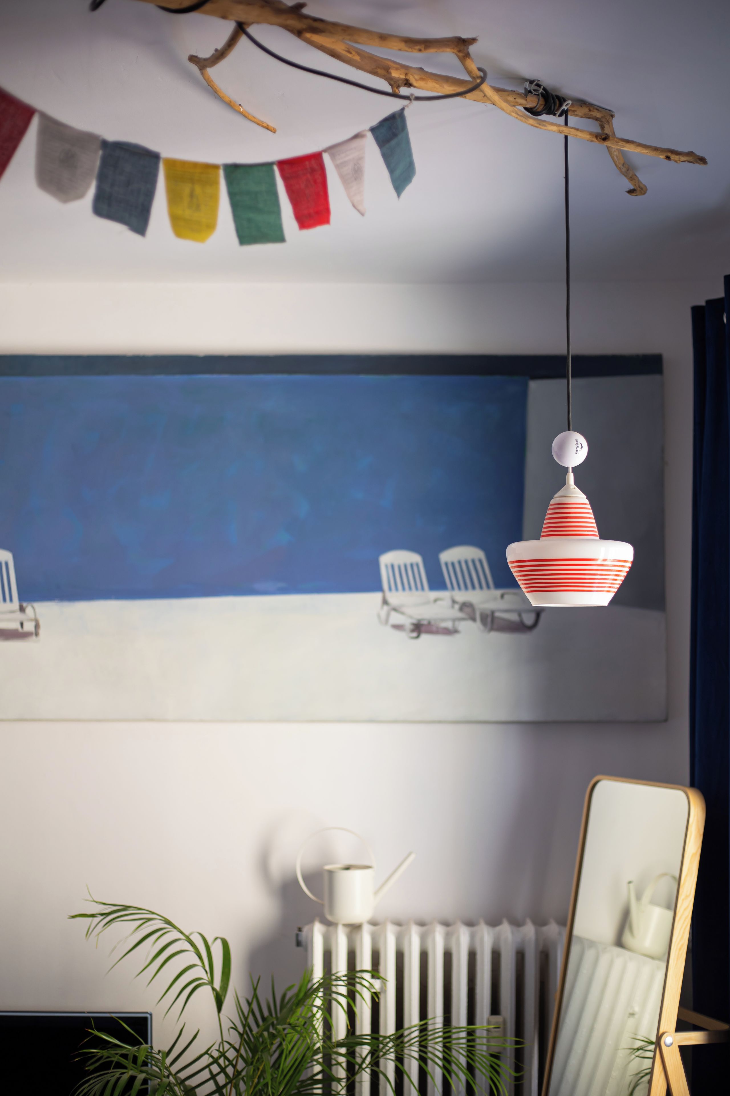 A room with a blue wall, a white radiator, a potted plant, a mirror, and a hanging light fixture.