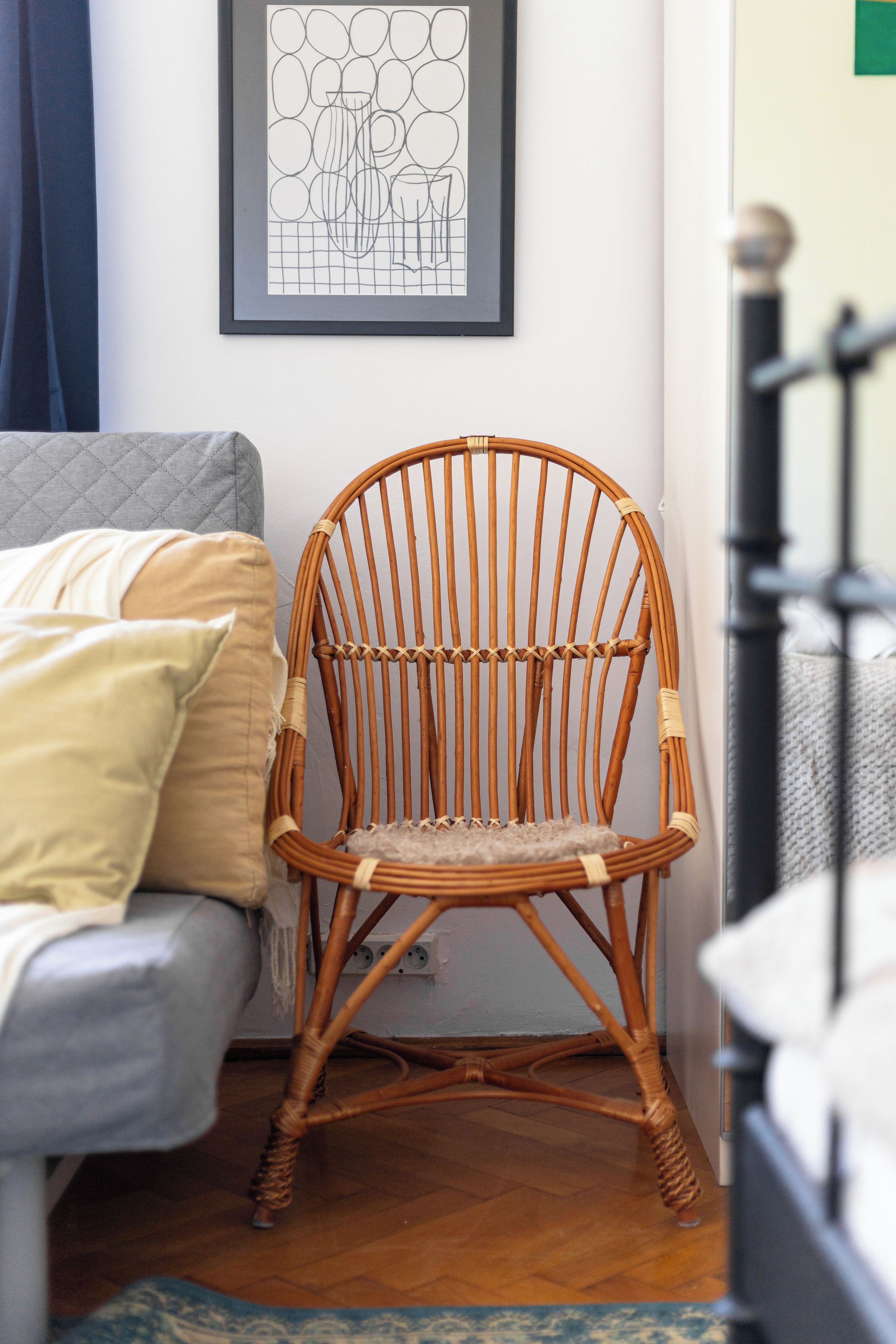A wicker chair in a room with a grey sofa, a framed abstract art piece on the wall, and a staircase in the background.