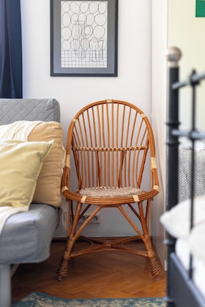 A wicker chair in a room with a grey sofa, a framed abstract art piece on the wall, and a staircase in the background. - Ikona Modernizmu w Stylu Boho (Poznań)