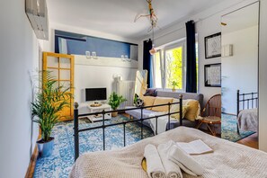 A modern bedroom with a bed, a sofa, a chair, a TV, and a window with curtains. - Ikona Modernizmu w Stylu Boho (Poznań)