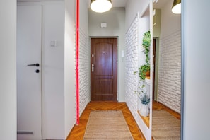 A hallway with a wooden door, white brick walls, a red trim, and a plant. - Ikona Modernizmu w Stylu Boho (Poznań)