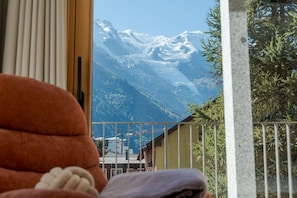 Blick auf Berge vom Balkon mit Geländer, ein Fenster mit Rollläden und ein Einblick in ein Gebäude mit einem Kran.