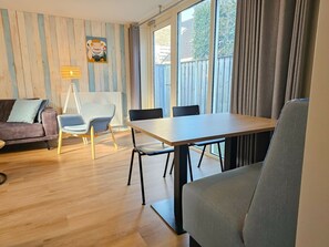 A modern living room with a wooden floor, a sofa, a dining table with chairs, and a large window with curtains. - Do36 Holiday Home With dog Domburg (Domburg)