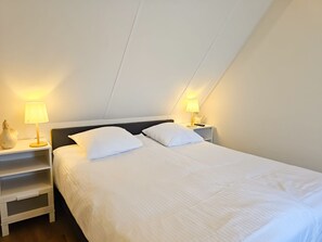 A single bed with white bedding in a room with a sloped ceiling, two bedside tables with lamps, and a white wall. - Do36 Holiday Home With dog Domburg (Domburg)