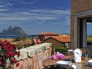 Eine Terrasse mit Blick auf einen Berg, ein Tisch gedeckt mit einer Schüssel, und ein Stuhl.