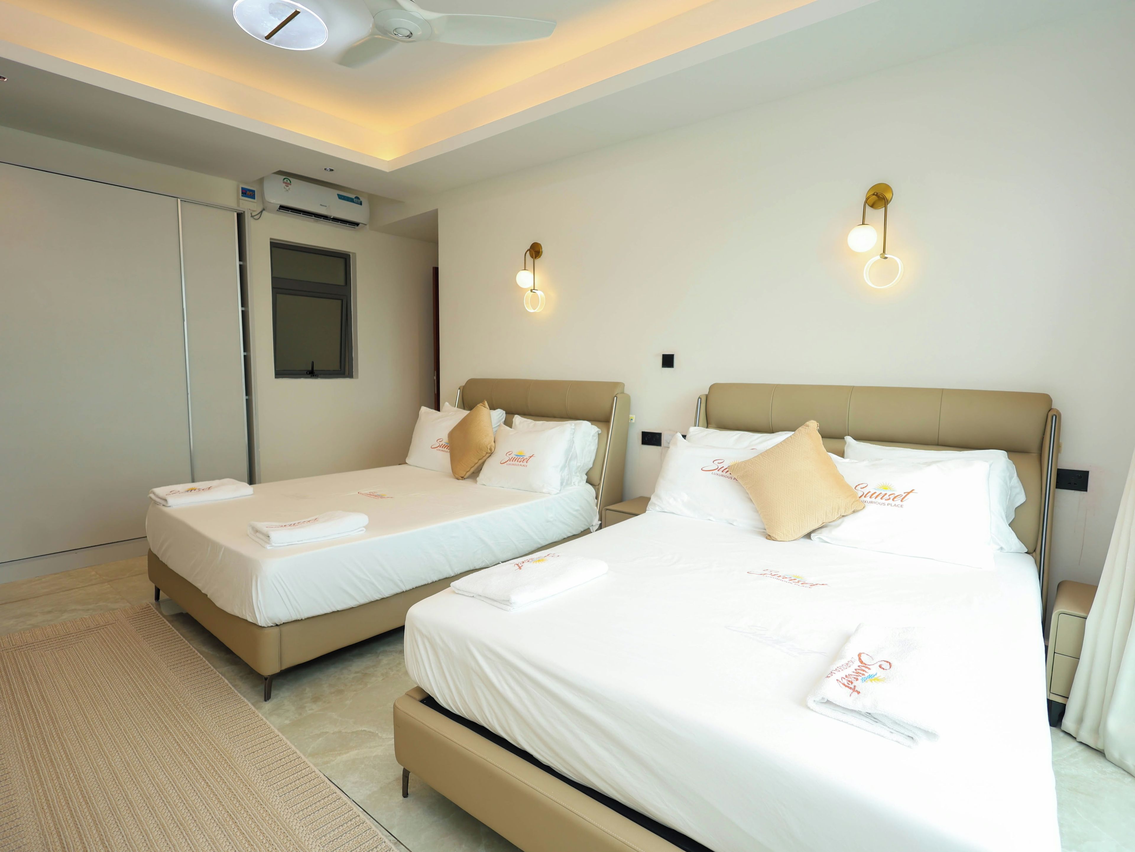 Ein Hotelzimmer mit zwei Betten, einem Deckenventilator, einer Klimaanlage und Wandleuchten.