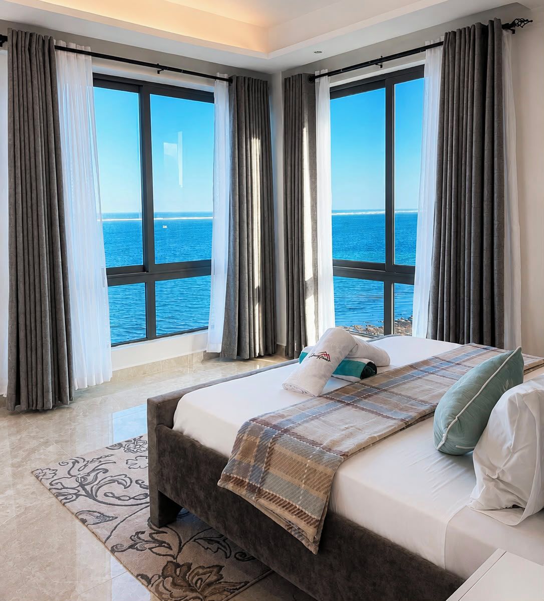 A hotel room with a large bed, a view of the sea, and a window with curtains.