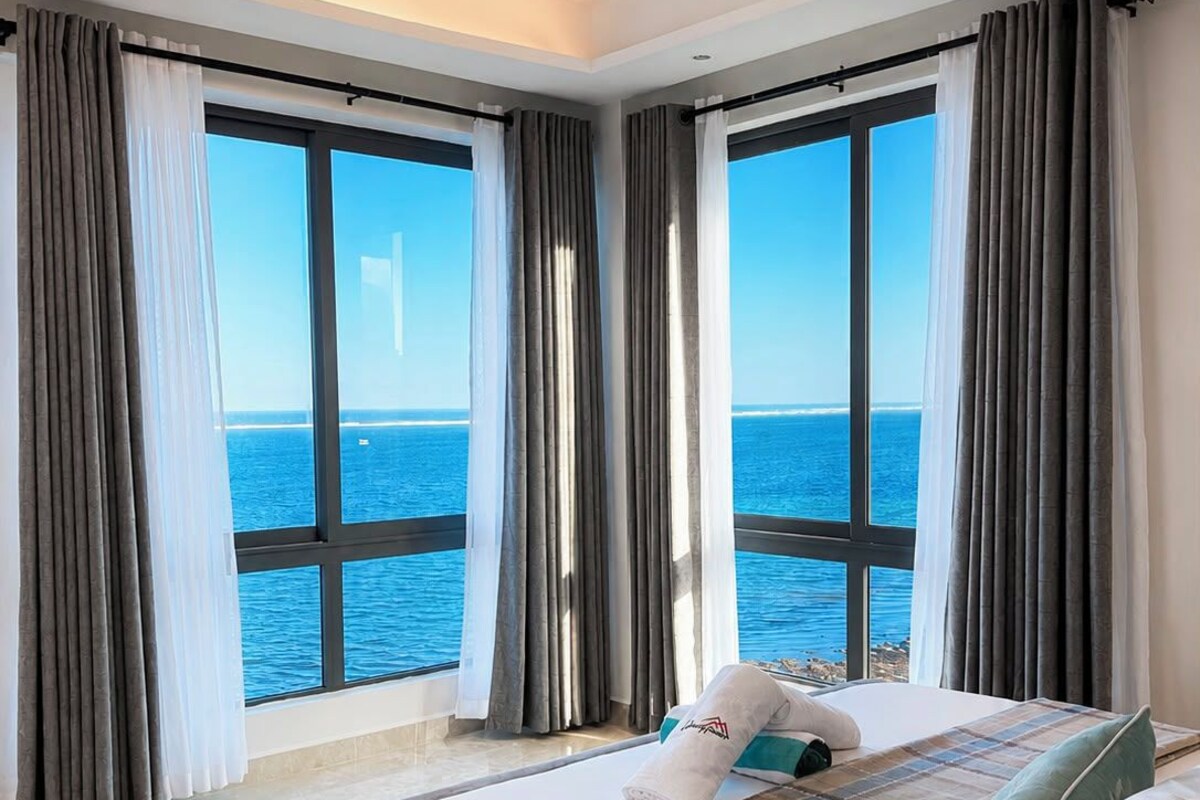 Ein Hotelzimmer mit einem großen Bett, Meerblick und einem Vorhangfenster.