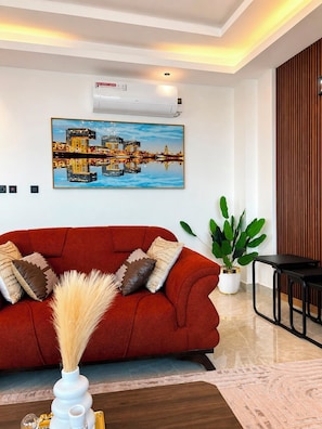 Ein modernes Wohnzimmer mit einem roten Sofa, einem Stadtbildgemälde, einer Klimaanlage, einer Topfpflanze und einem schwarzen Tisch.