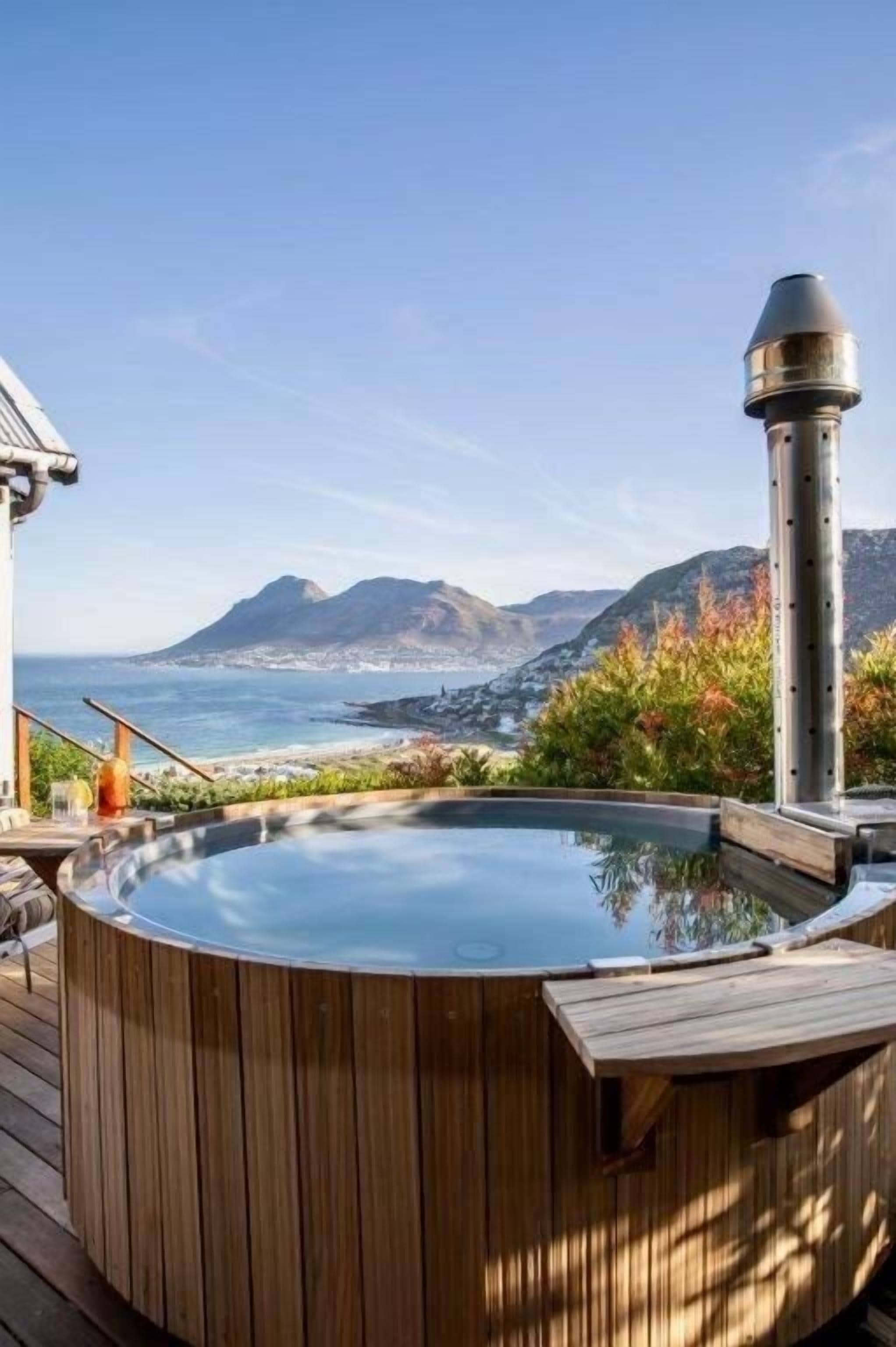 A hot tub on a wooden deck with a view of the ocean and mountains.