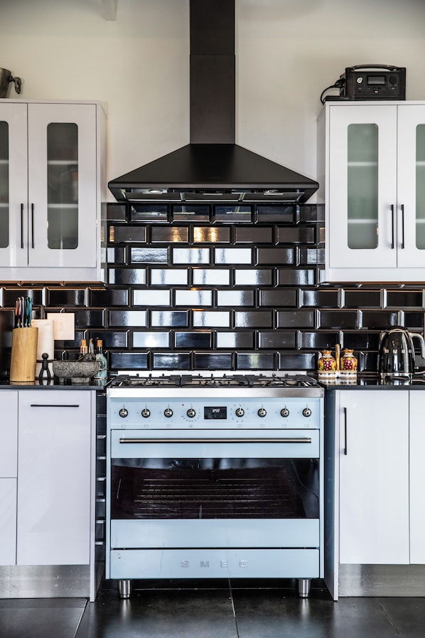 Una cocina con extractor de acero inoxidable, horno empotrado y muebles de color blanco.
