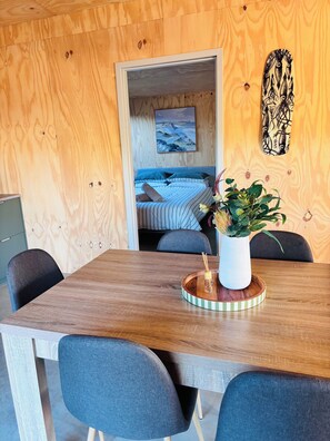 A wooden interior with a dining table, chairs, a bed with striped bedding, a painting, and a wall decoration. - Red Earth Retreat - raw,natural timber home (Kalbarri)
