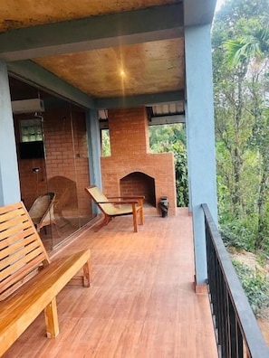 Un espacio al aire libre techado con una chimenea de ladrillo, mobiliario de madera y vistas a la vegetación.