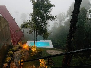 Un área de piscina con un edificio de techo rojo, rodeado de árboles y vegetación.