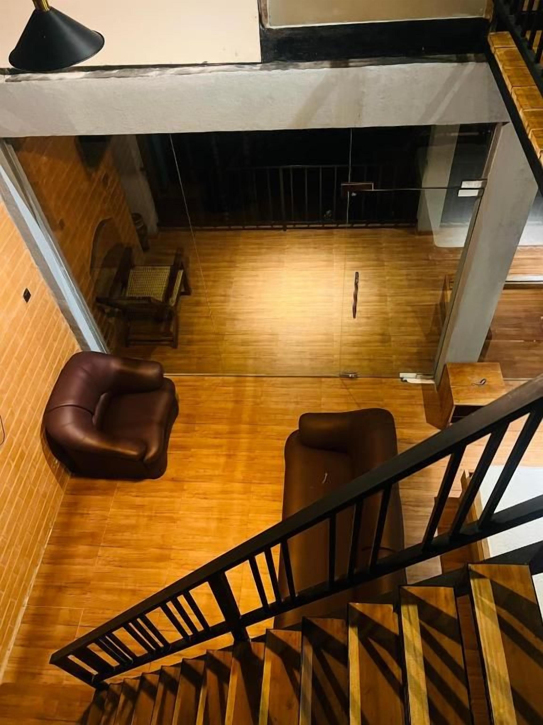 A wooden-floored room with a staircase, a brown leather chair, and a small table.