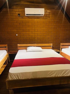 Une pièce avec trois lits en bois, une couverture rouge et un appareil de climatisation fixé au mur.