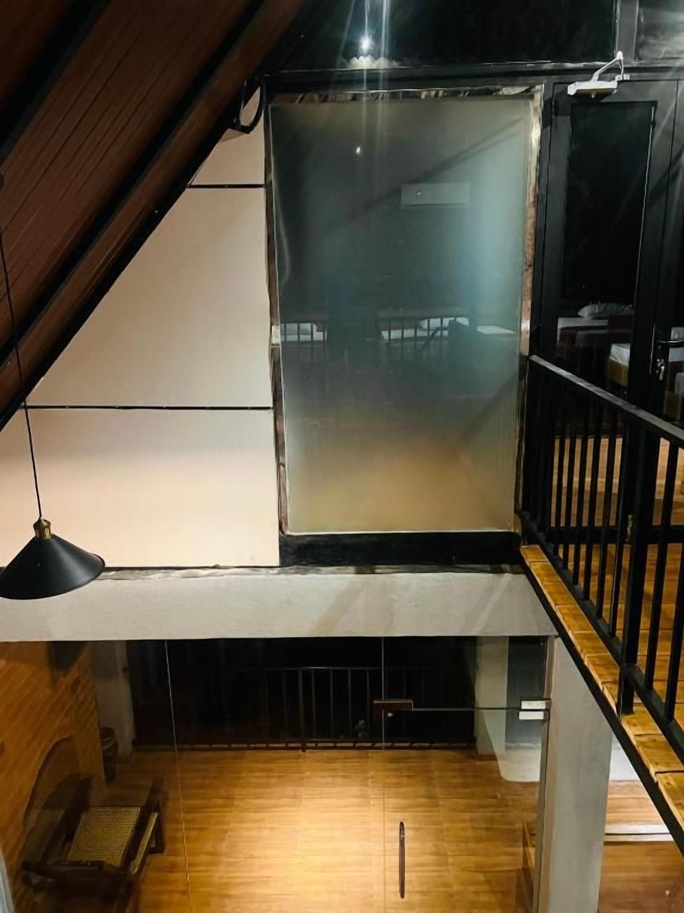 A room with a sloped ceiling, a wooden floor, a black railing, and a hanging light fixture.