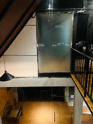Une pièce avec un plafond en pente, un plancher en bois, une rambarde noire et un luminaire suspendu.