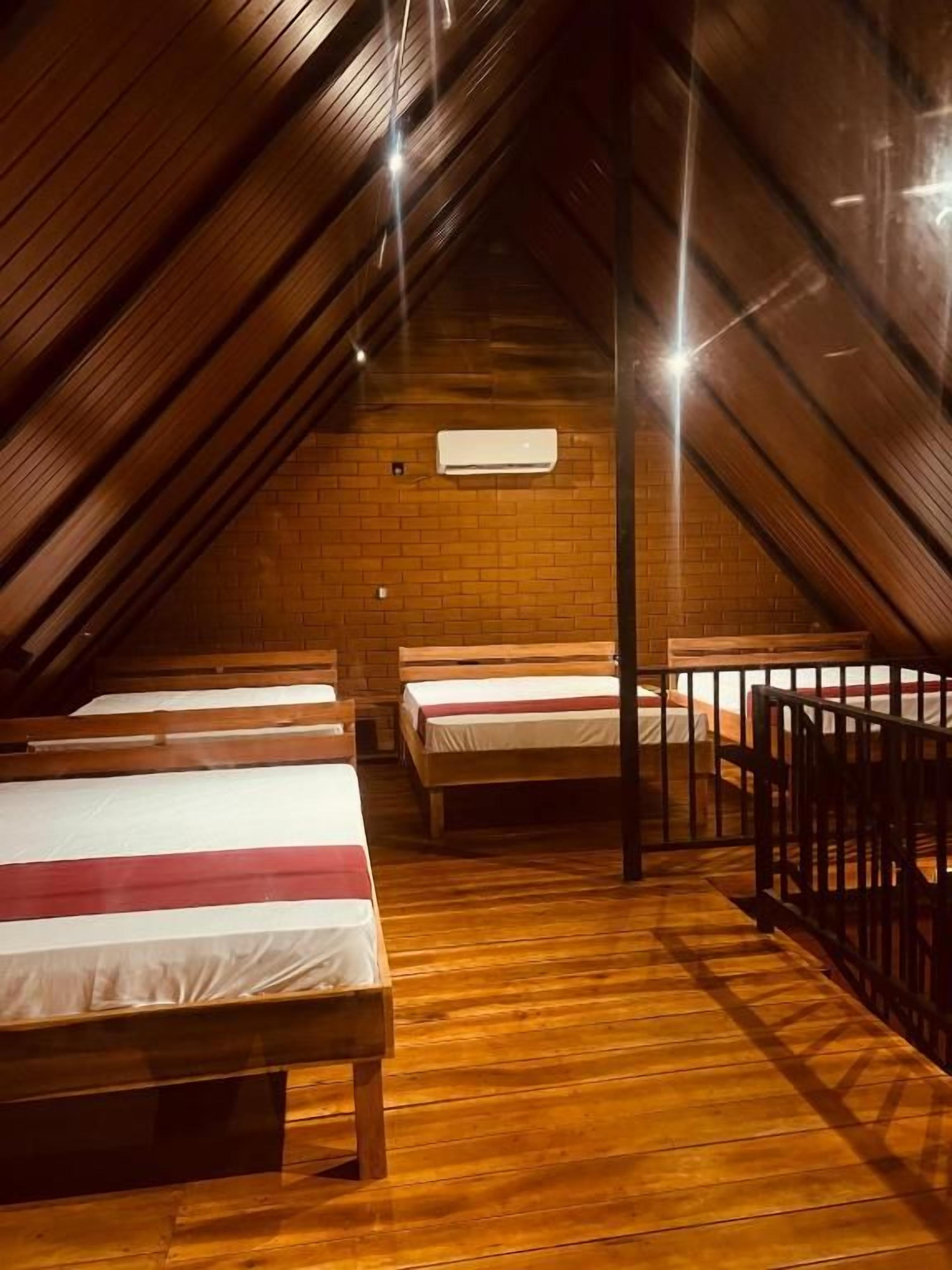 A room with wooden floors and sloped ceilings, featuring three beds with white and red bedding.