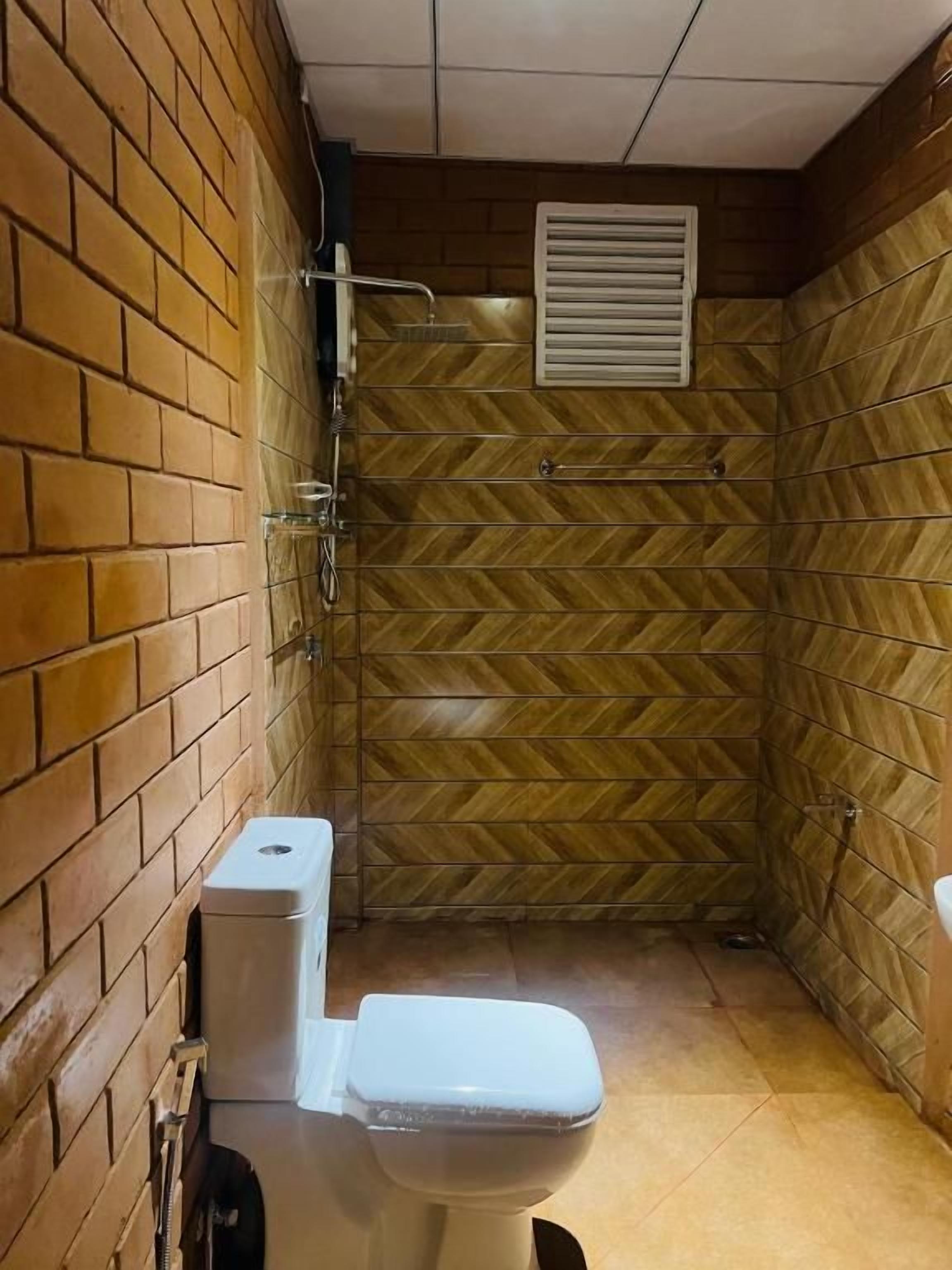 A small, enclosed bathroom with a toilet, shower, and a herringbone-patterned wall.