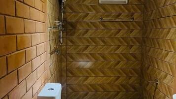 A small, enclosed bathroom with a toilet, shower, and a herringbone-patterned wall.